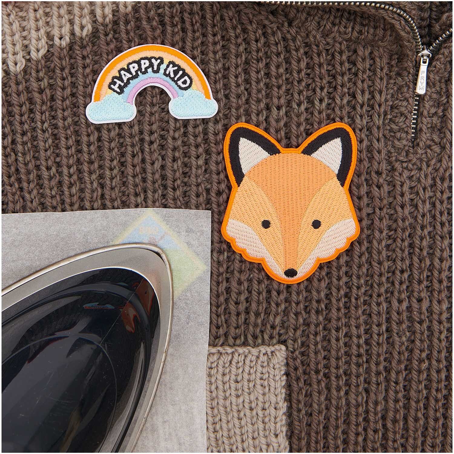 Patches Pfadfinder Fuchs zum Aufbügeln von Rico Design auf braunem Strickpullover mit Bügeleisen.