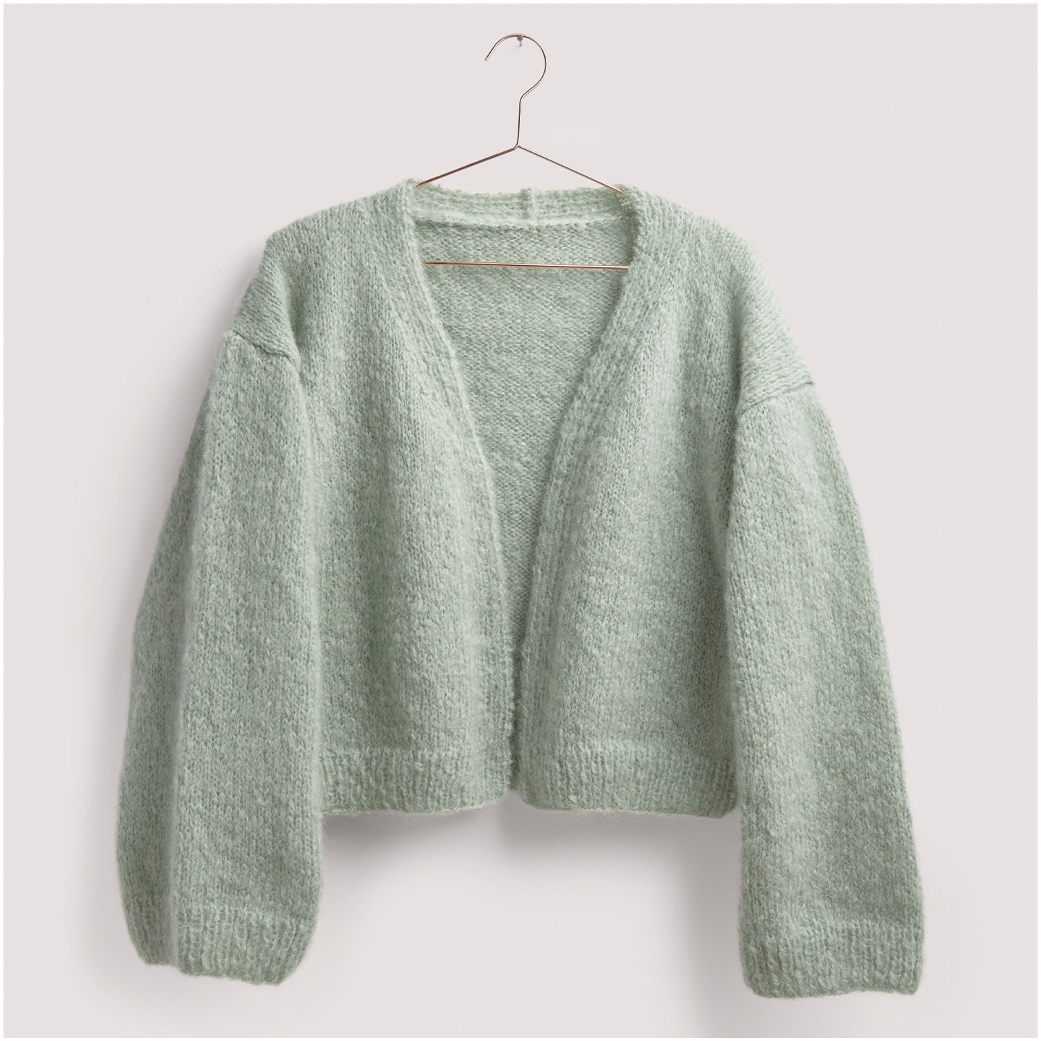 Strickset Jacke Modell 01 aus Die Neue Masche Nr. 8: Weiche, mintgrüne Strickjacke auf einem Kleiderbügel vor neutralem Hintergrund.