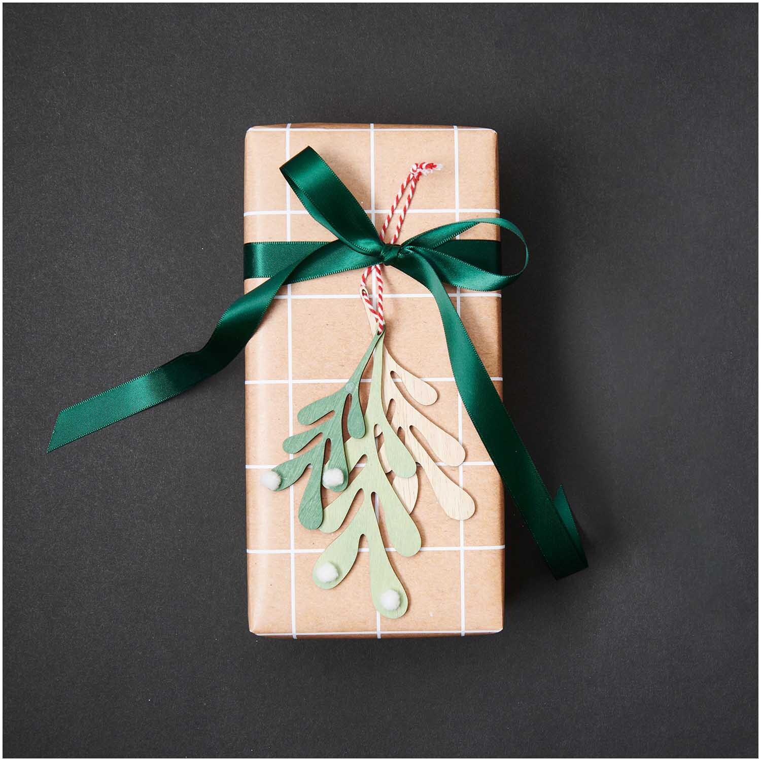 Holzhänger Blätter mit Pompons an einem Geschenk mit grünem Band, dekoriert von Rico Design.