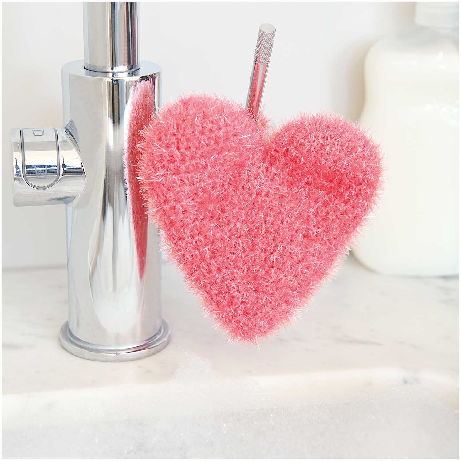 Creative Bubble: Herzförmiger, pinker Schwamm von Rico Design, dekorativ an einem Wasserhahn hängend.