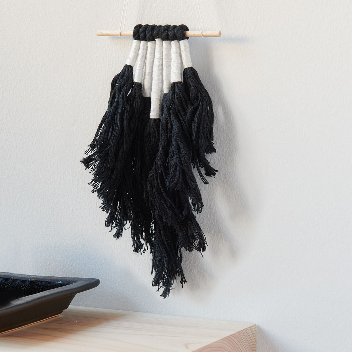 Bastelanleitung stylisher Wandbehang in Schwarz-Weiß: Dekorativer Makramee-Wandbehang mit Fransen an Holzstab, ideal für moderne Wohnräume.
