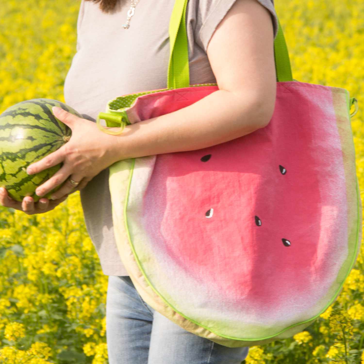 Wassermelonen-Tasche in leuchtendem Rot und Grün, getragen von Person in blühendem Feld.