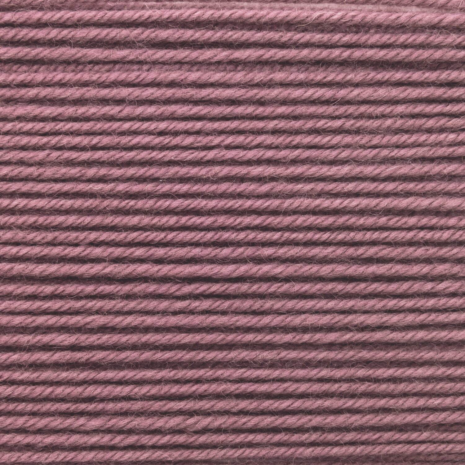 Essentials Merino dk, feine mitteldicke Wolle von Rico Design in holunderfarbenem Ton, detailreiche Nahaufnahme der glatten Fäden, 50g 110m Knäuel