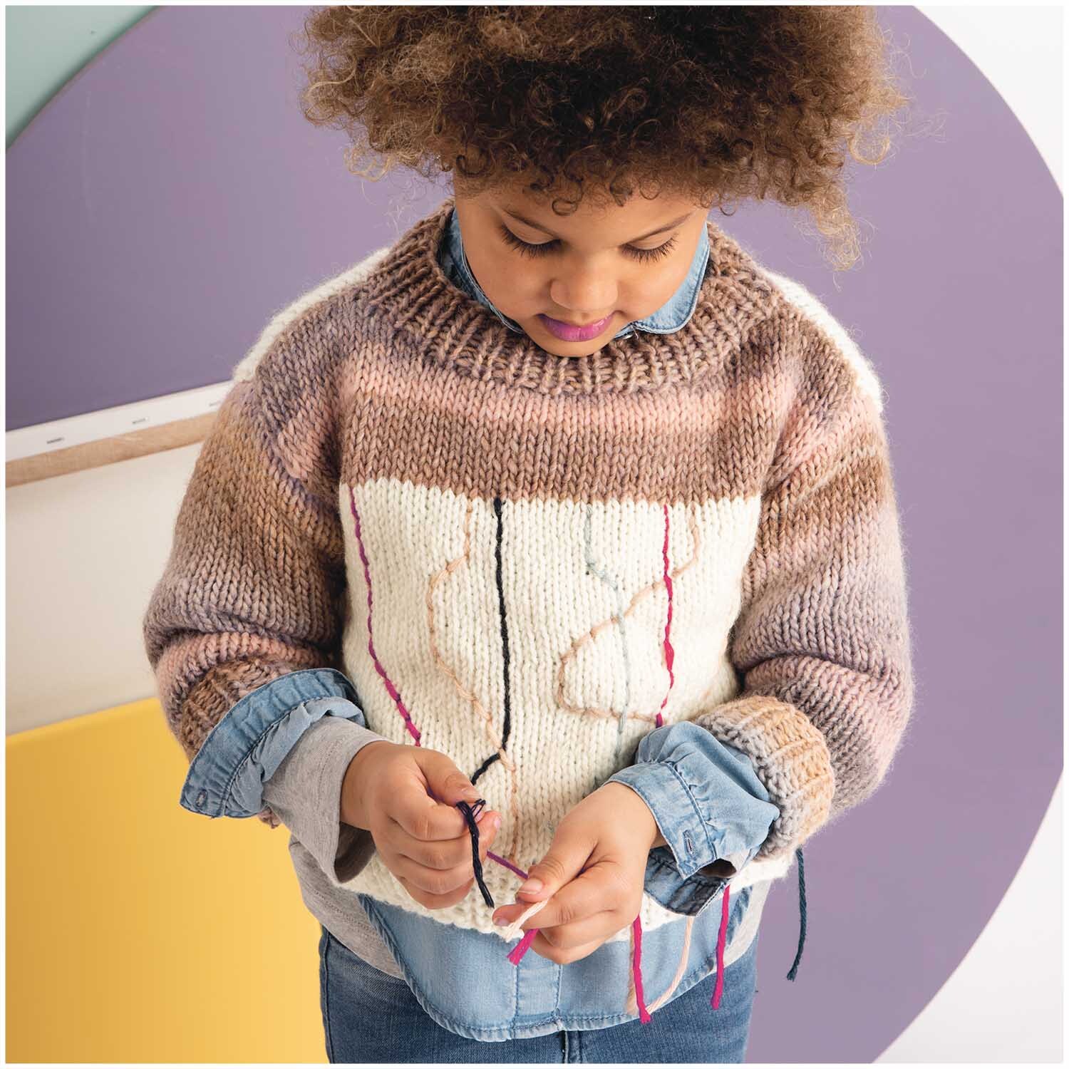 Essentials Alpaca Blend chunky Pullover in Creme- und Marinefarben, getragen von einem Kind, das mit Garn spielt.