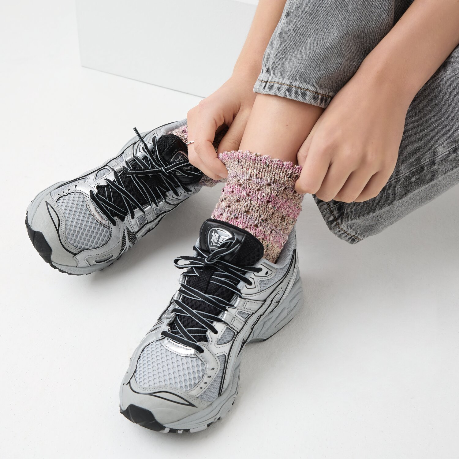 Strickset Socken Modell 14b: Person zieht bunte Socken an, trägt graue Sneakers und Jeans.