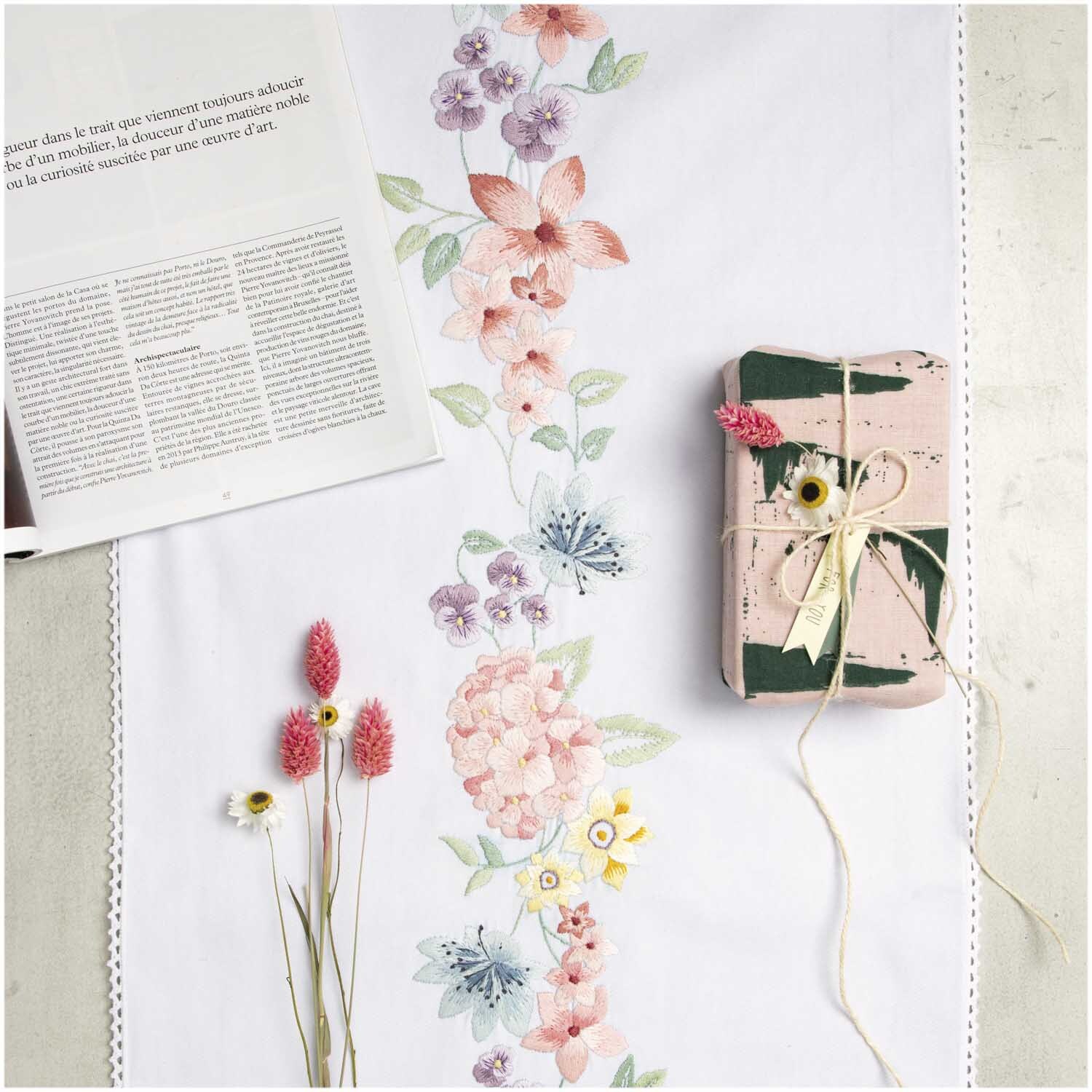 Stickpackung Läufer Hortensienkranz 45x150cm zeigt florales Design auf weißem Stoff, dekoriert mit Buch und Blumen.