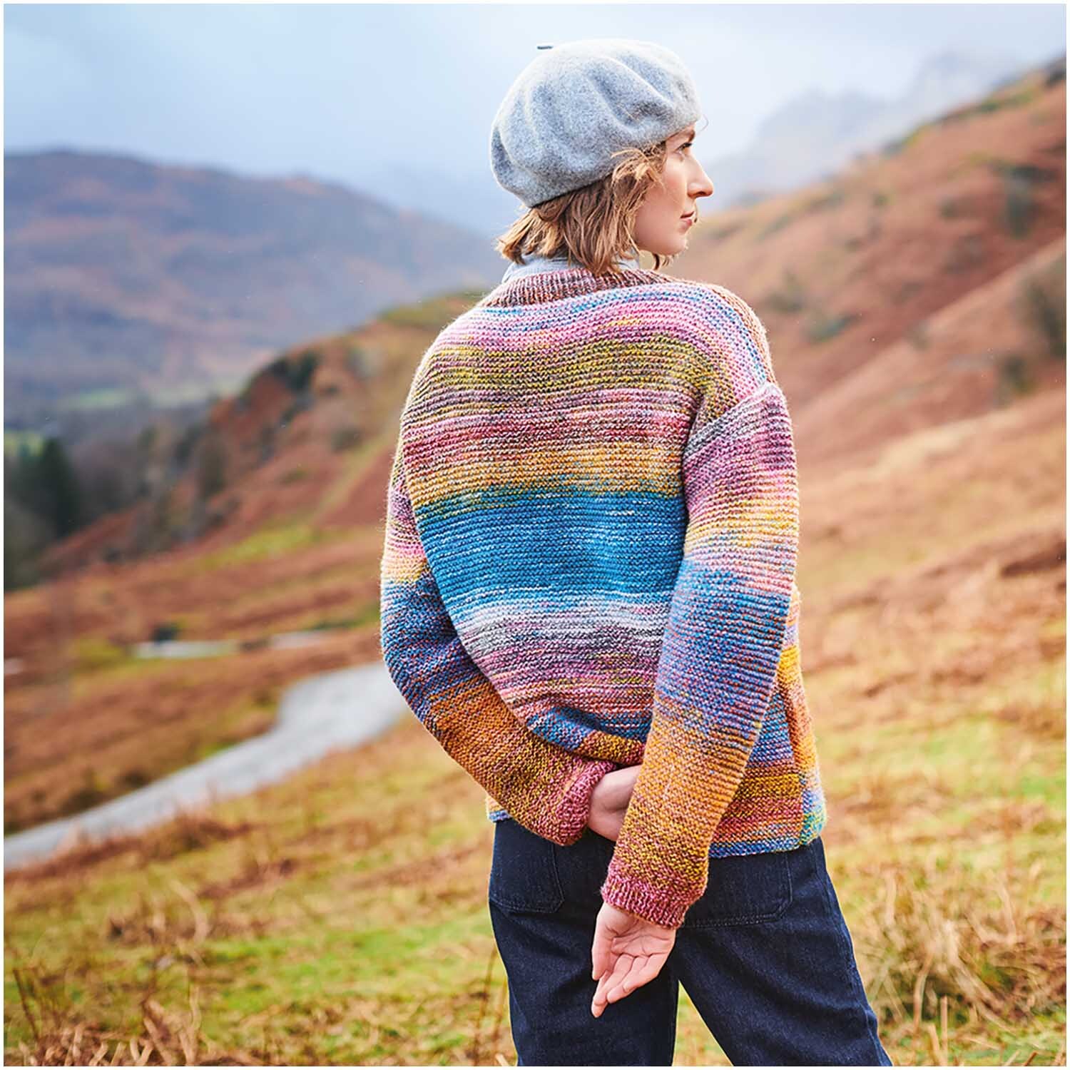 Strickset Pullover Modell 15: Bunter Pullover aus Chic Unique dk Special, getragen in bergiger Landschaft.