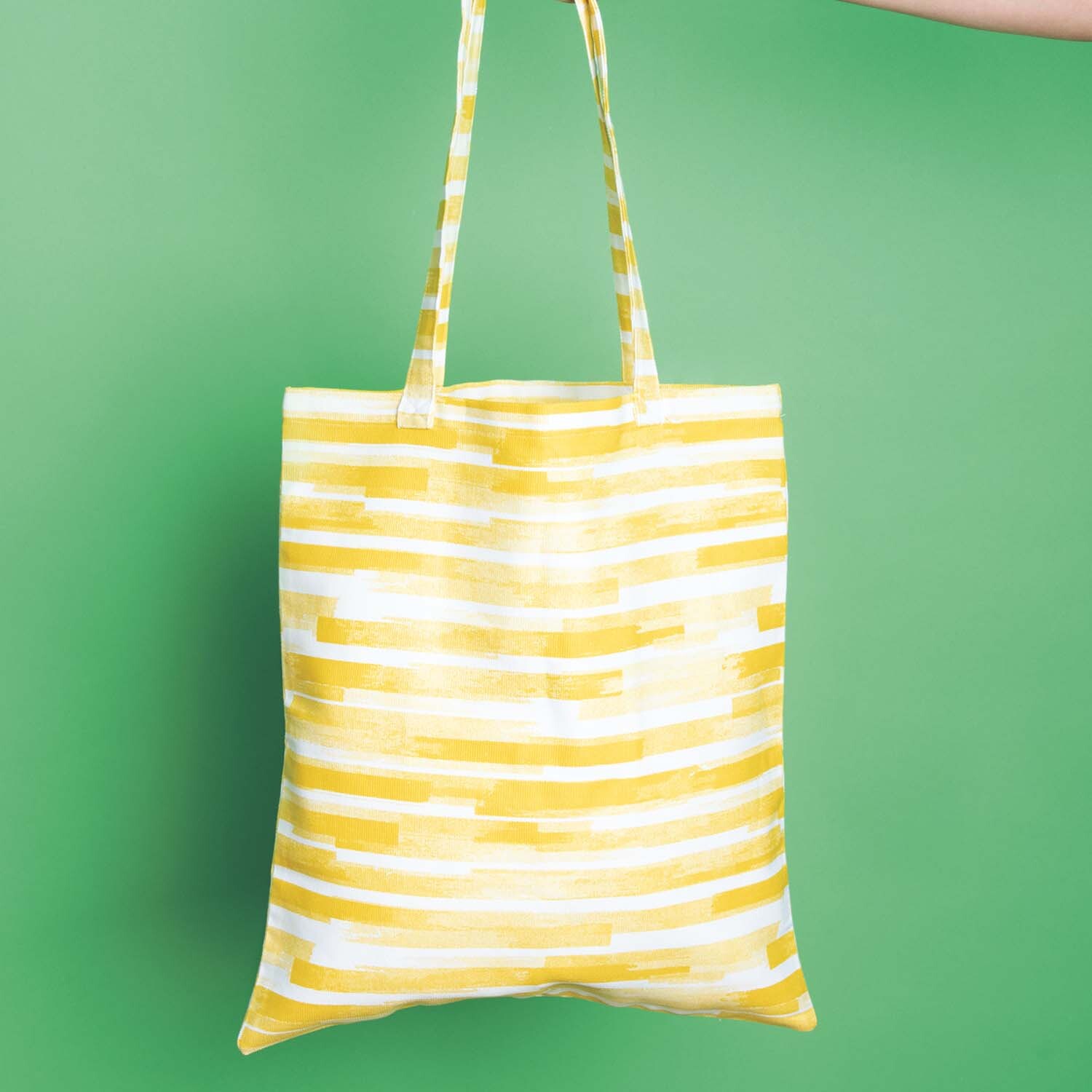 Nähanleitung Tasche aus Canvas-Stoff: Gelbe gestreifte Tasche vor grünem Hintergrund, handgehalten.