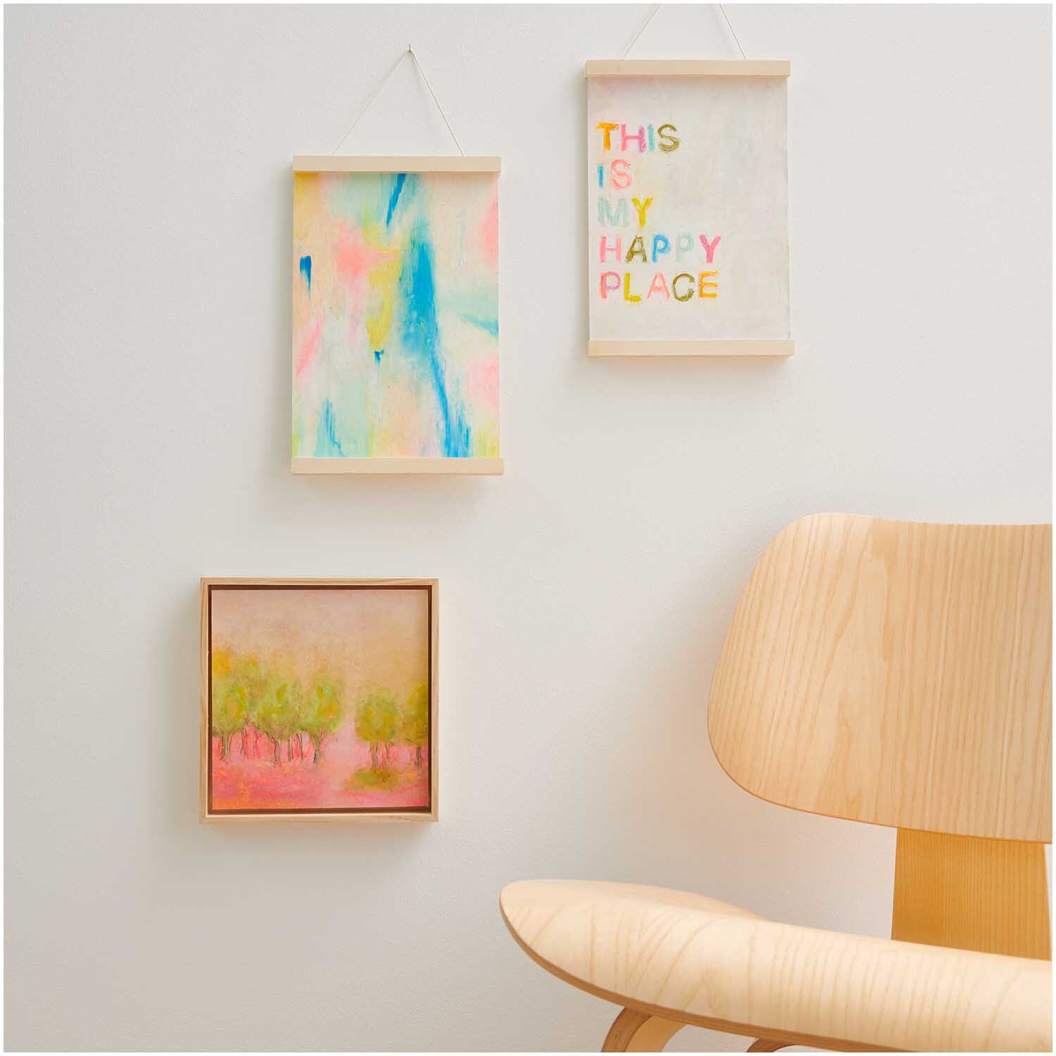 Ölpastellkreide 36 Farben von Rico Design: Drei bunte Bilder an einer weißen Wand über einem Holzstuhl.