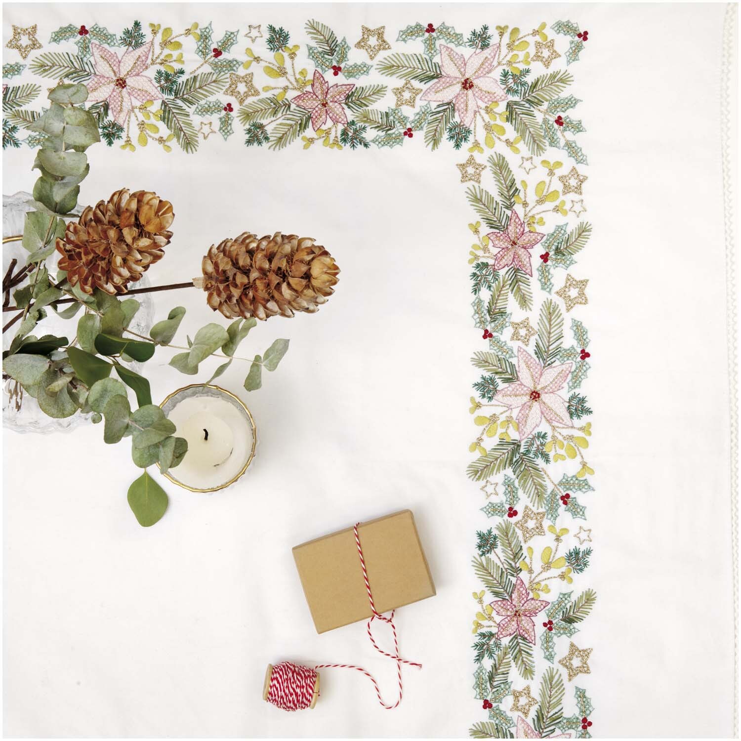 Stickpackung Tischdecke Weihnachtssterne 95x95cm mit festlichem Muster aus Sternen und Blättern, dekoriert mit Kerze und Geschenk.