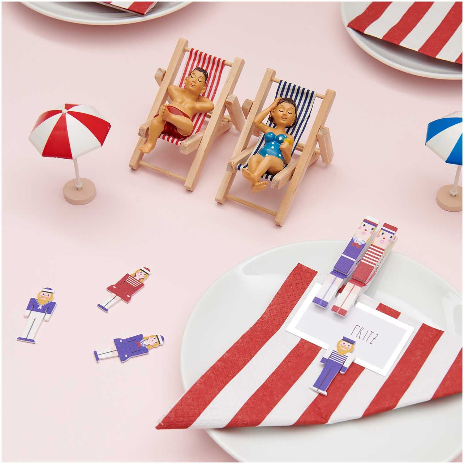 Deko-Figur Urlauber 8x5cm: Zwei Miniatur-Urlauber in Liegestühlen mit rot-weiß gestreiften Handtüchern und kleinen Sonnenschirmen.