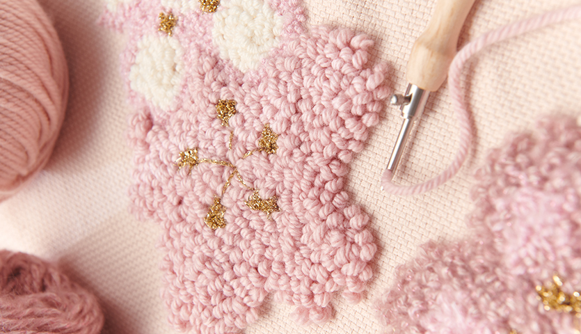 Anleitung Kissen mit Kirschblüten punchen: Nahaufnahme eines rosa Kirschblütenmusters mit Punchneedle und Garn.