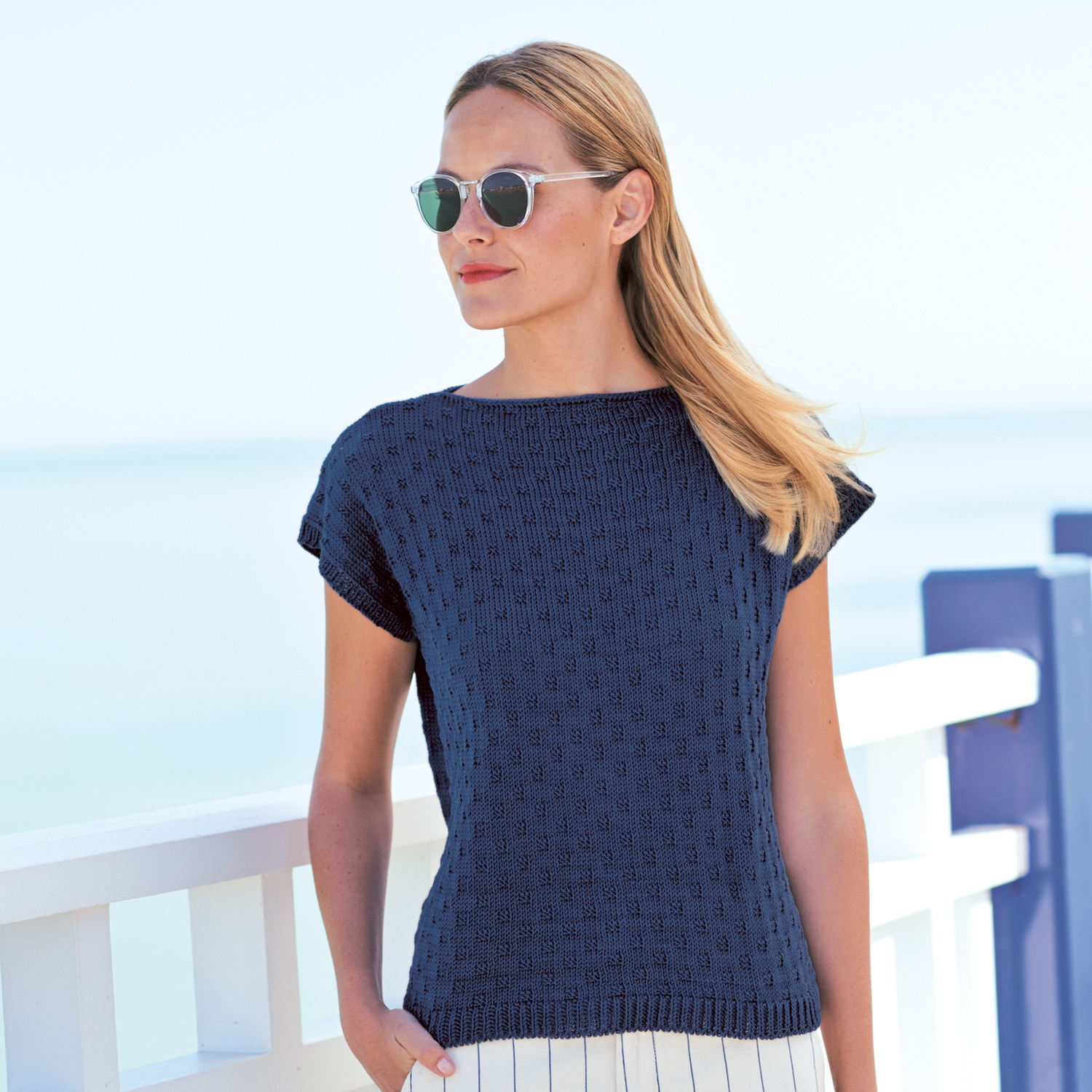 Strickanleitung Top aus Mille Fili: Frau trägt ein elegantes, dunkelblaues Stricktop am Strand.