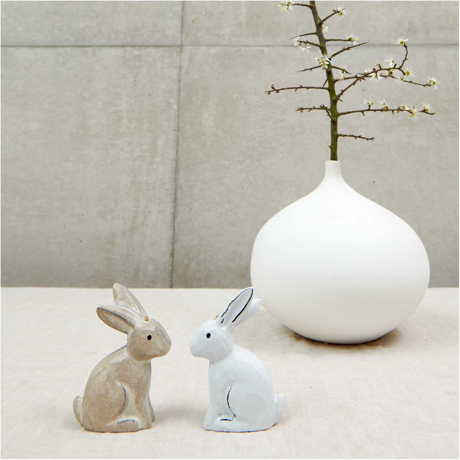 Holzanhänger Hase groß weiß 1 Stück: Zwei Hasenfiguren, eine weiß, eine natur, vor weißer Vase.