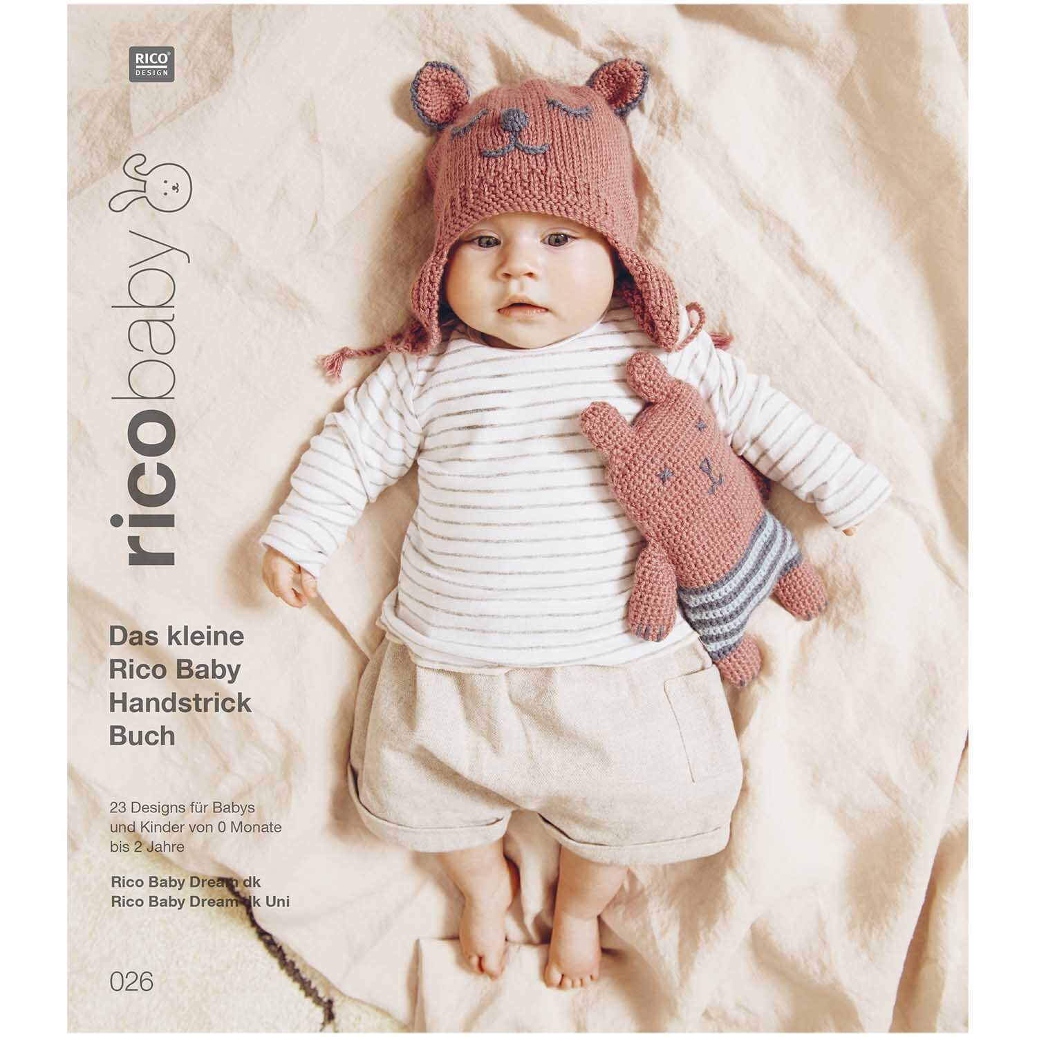 Rico Baby Heft Nr.26 zeigt ein Baby in gestrickter Kleidung mit Mütze und Kuscheltier auf beigem Hintergrund.