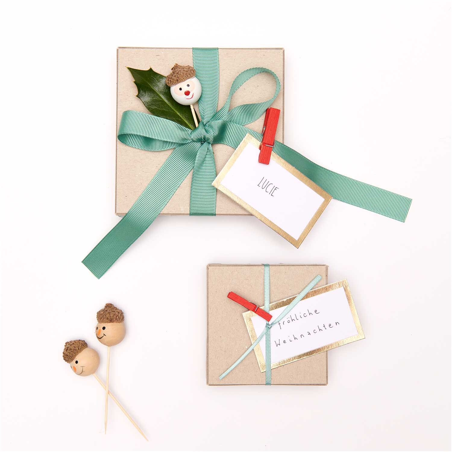 Sticks Weihnachtsmann weiß 3 Stück: Zwei dekorierte Geschenke mit grünen Schleifen und Weihnachtsmann-Sticks.