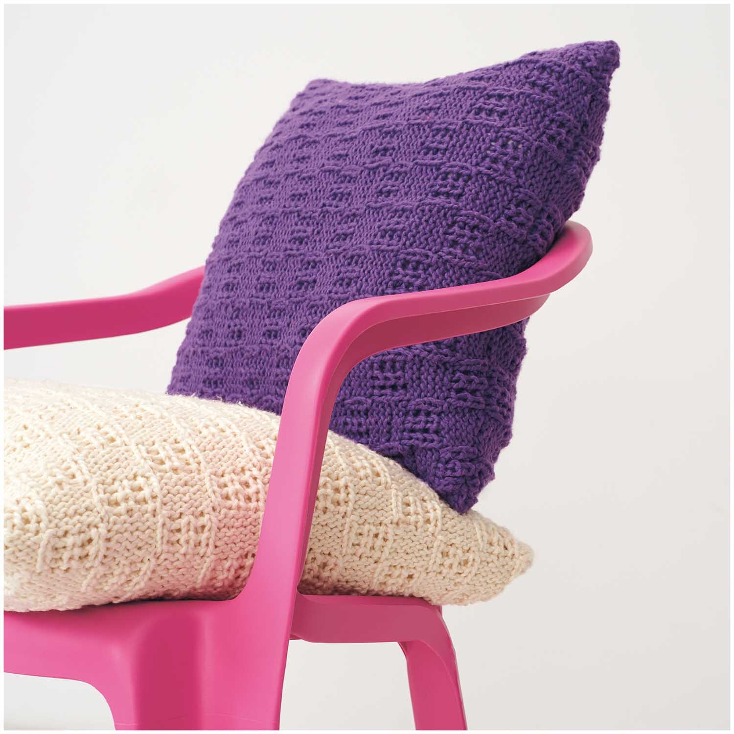 Creative So Cool + So Soft Cotton chunky: Lila gestricktes Kissen auf pinkem Stuhl, darunter cremefarbenes Kissen. Ideal für stilvolle Wohnräume.