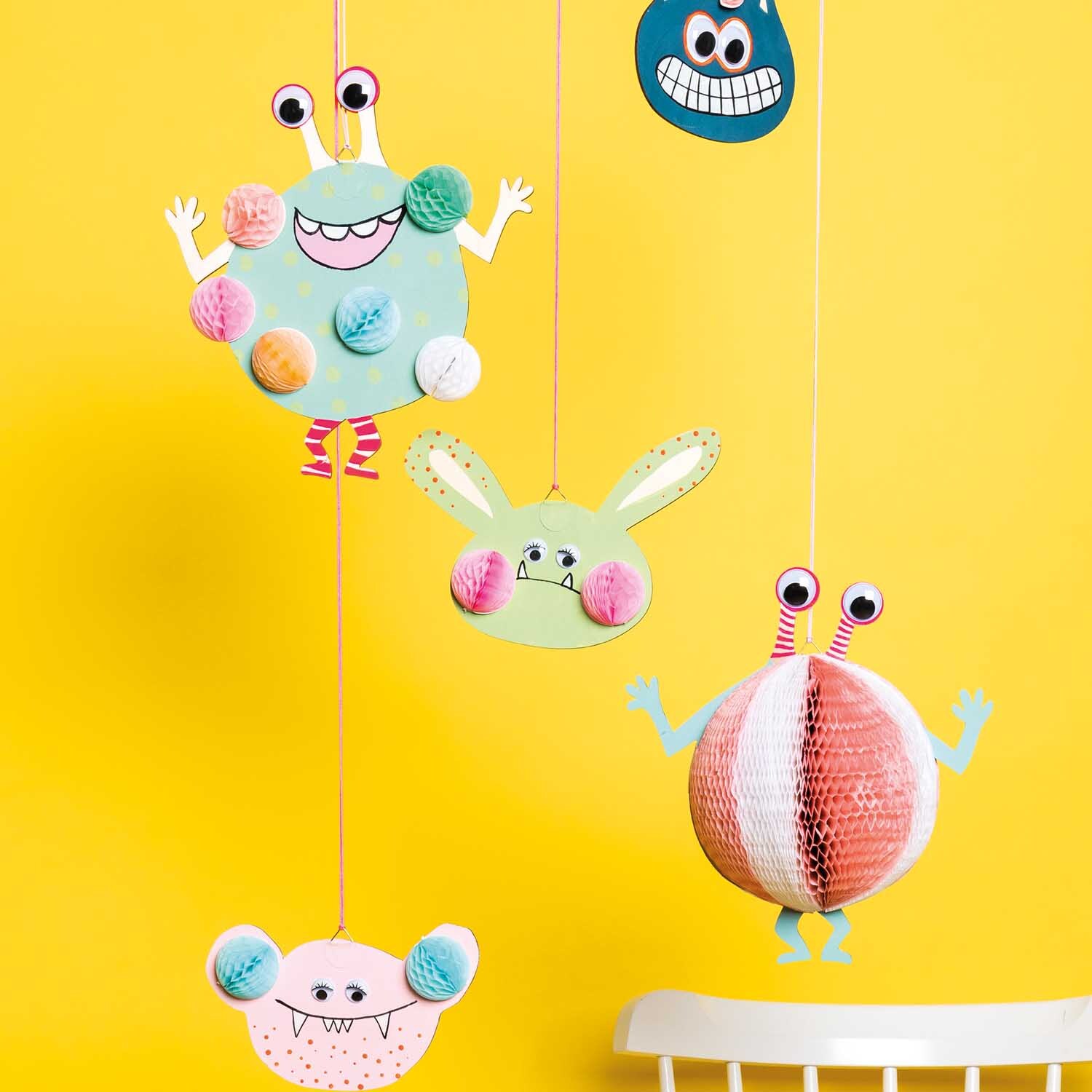 Bastelanleitung Monster-Mobilé aus Wall Charms: Bunte Monster aus Papier hängen vor gelbem Hintergrund.
