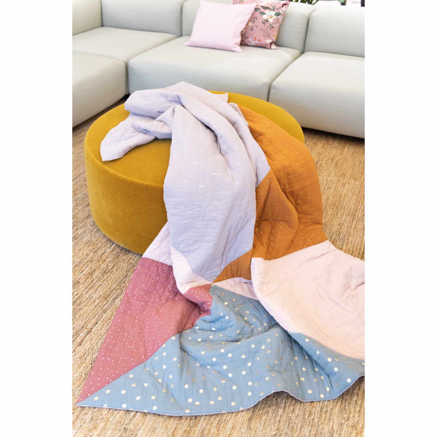 Krinkelmusselin-Druckstoff altrosa Hot Foil 130cm: Bunte Decke auf gelbem Hocker, kombiniert mit Sofa im Hintergrund.