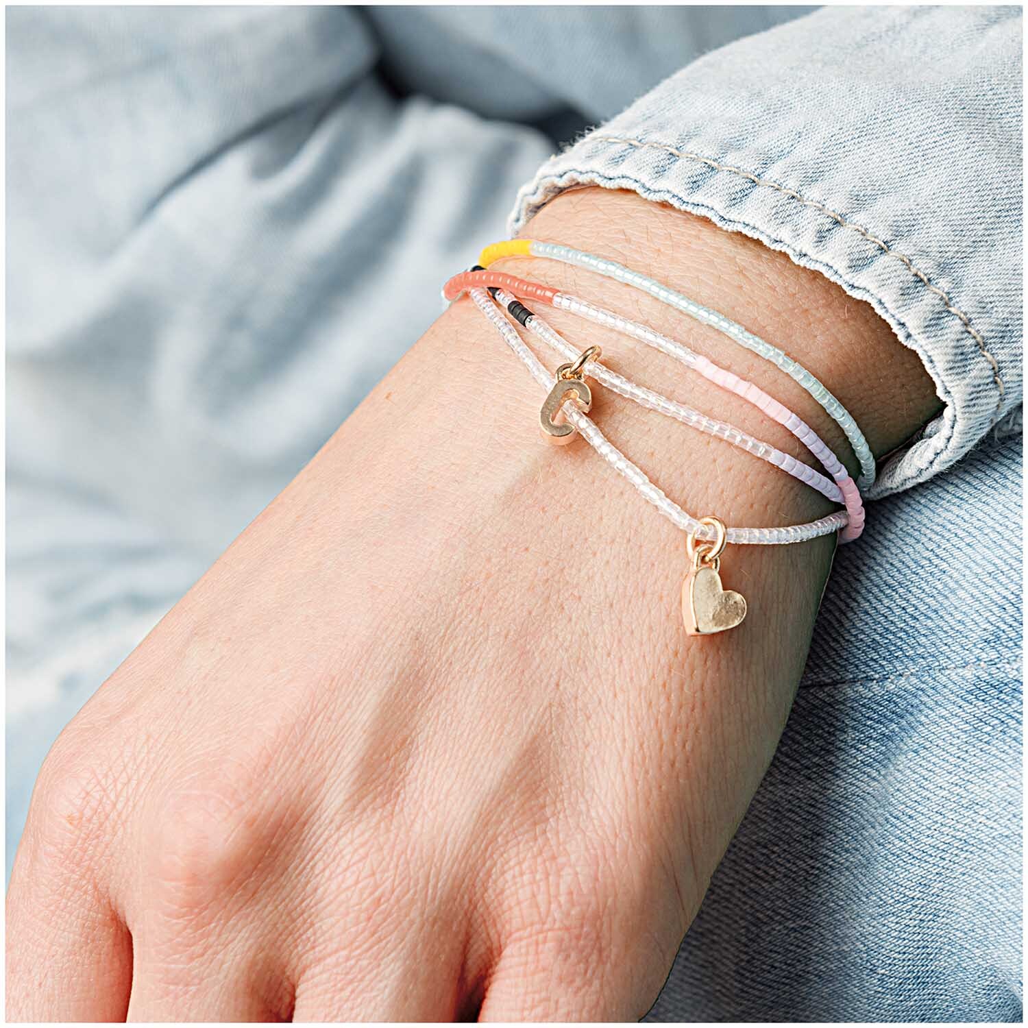 Anhänger Herz gold: Zarte Armbänder mit goldenen Herzanhängern von Rico Design auf einem Handgelenk.