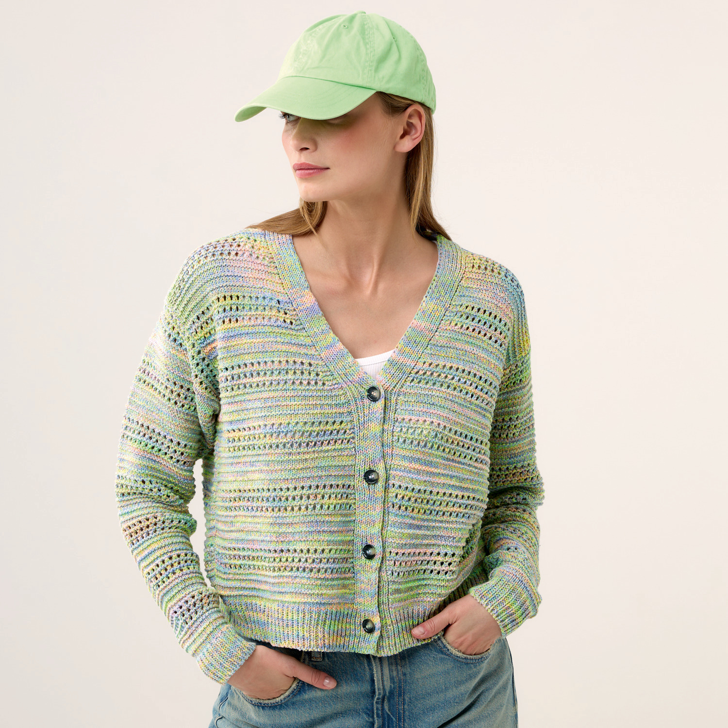 Strickset Jacke Modell 30 aus Die Neue Masche Nr. 9: Bunte Strickjacke mit Knöpfen, kombiniert mit grüner Kappe und Jeans.