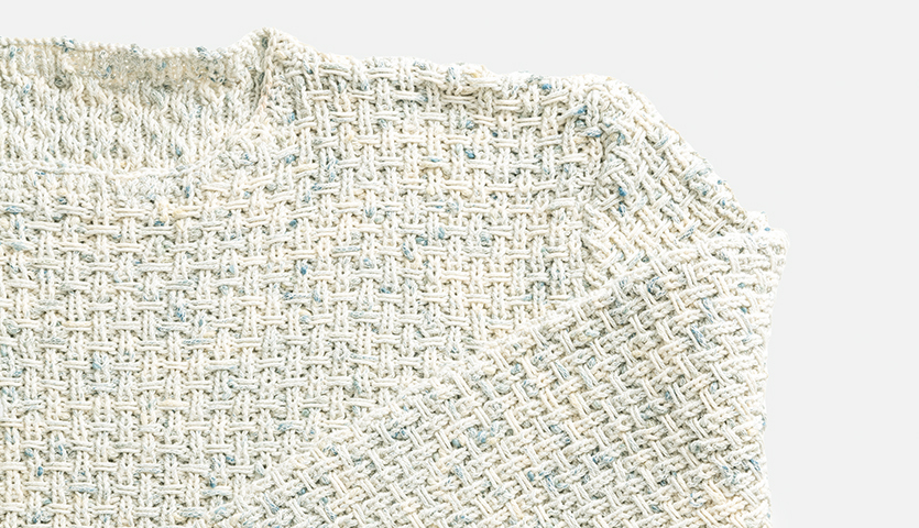 Strickanleitung Pullover aus Fashion Cotton Neps dk: Nahaufnahme eines cremefarbenen Strickpullovers mit feinem Muster.