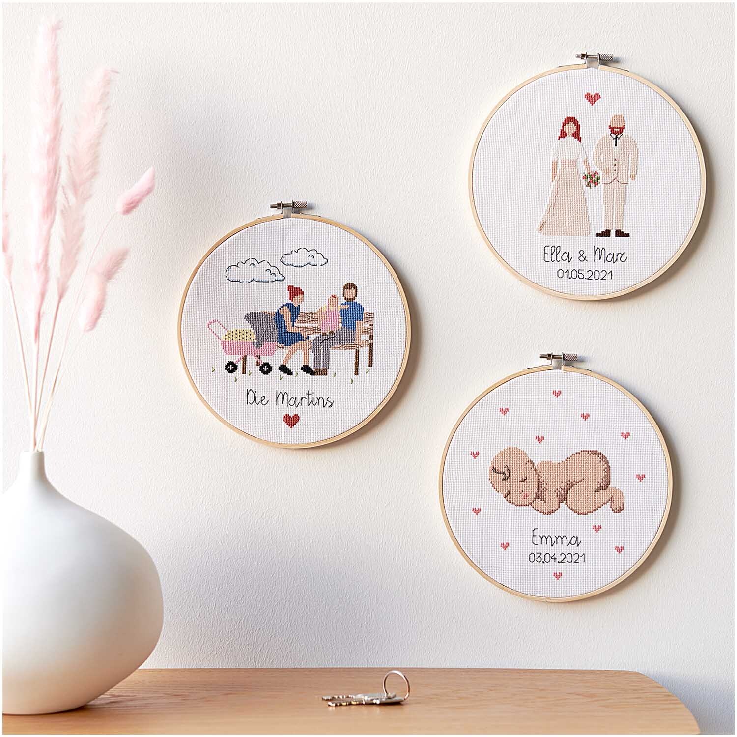 Figurico Stickpackung Young Family 20cm zeigt drei bestickte Rahmen mit Familienmotiven an einer Wand.