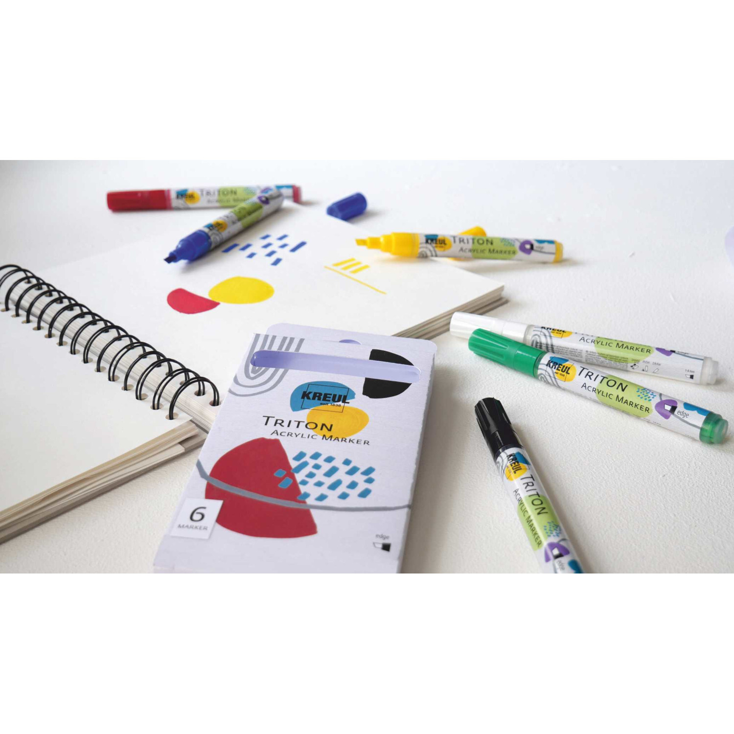 TRITON Acrylic Paint Marker 1-4mm, 6-teilig, in verschiedenen Farben auf einem Tisch mit Skizzenbuch.