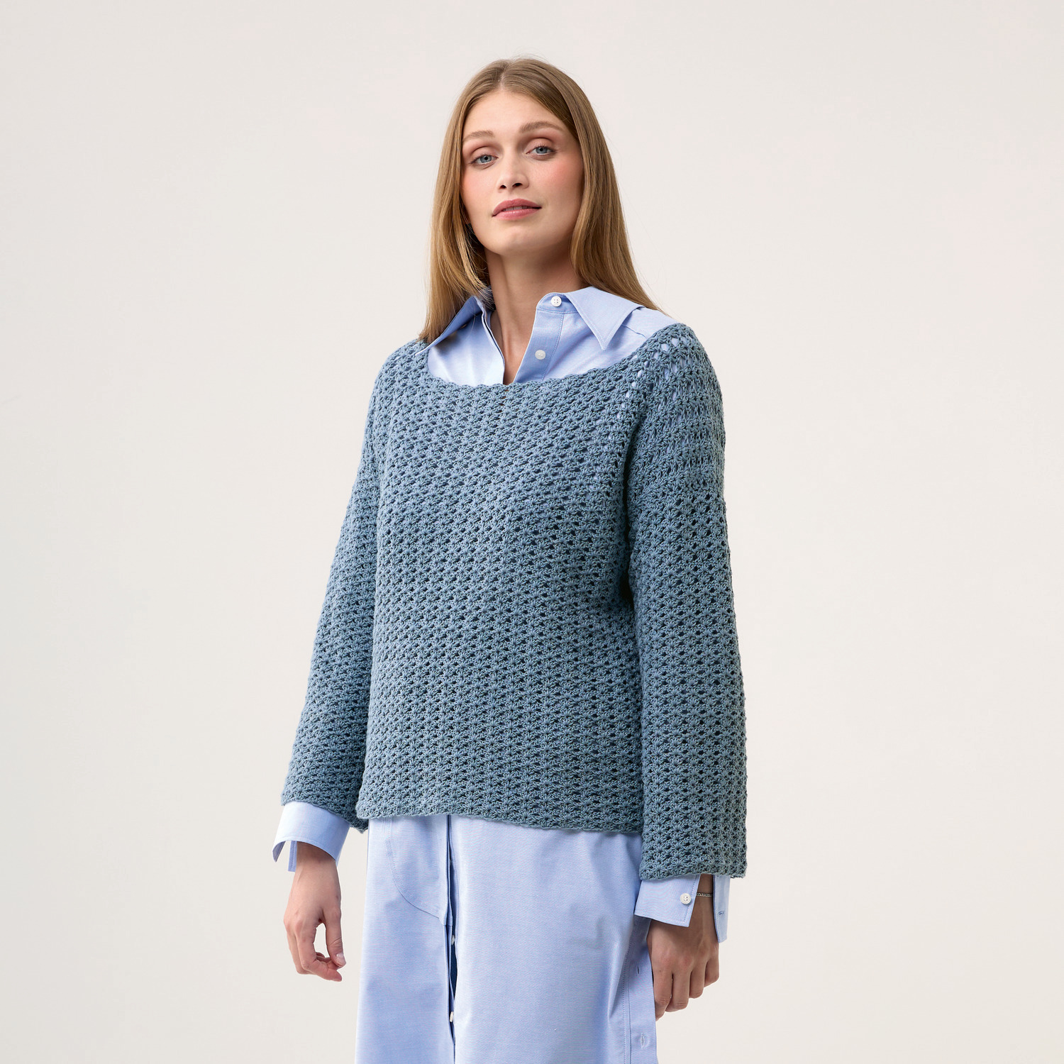 Häkelset Pullover Modell 23: Frau trägt blauen, gehäkelten Pullover über hellblauer Bluse.