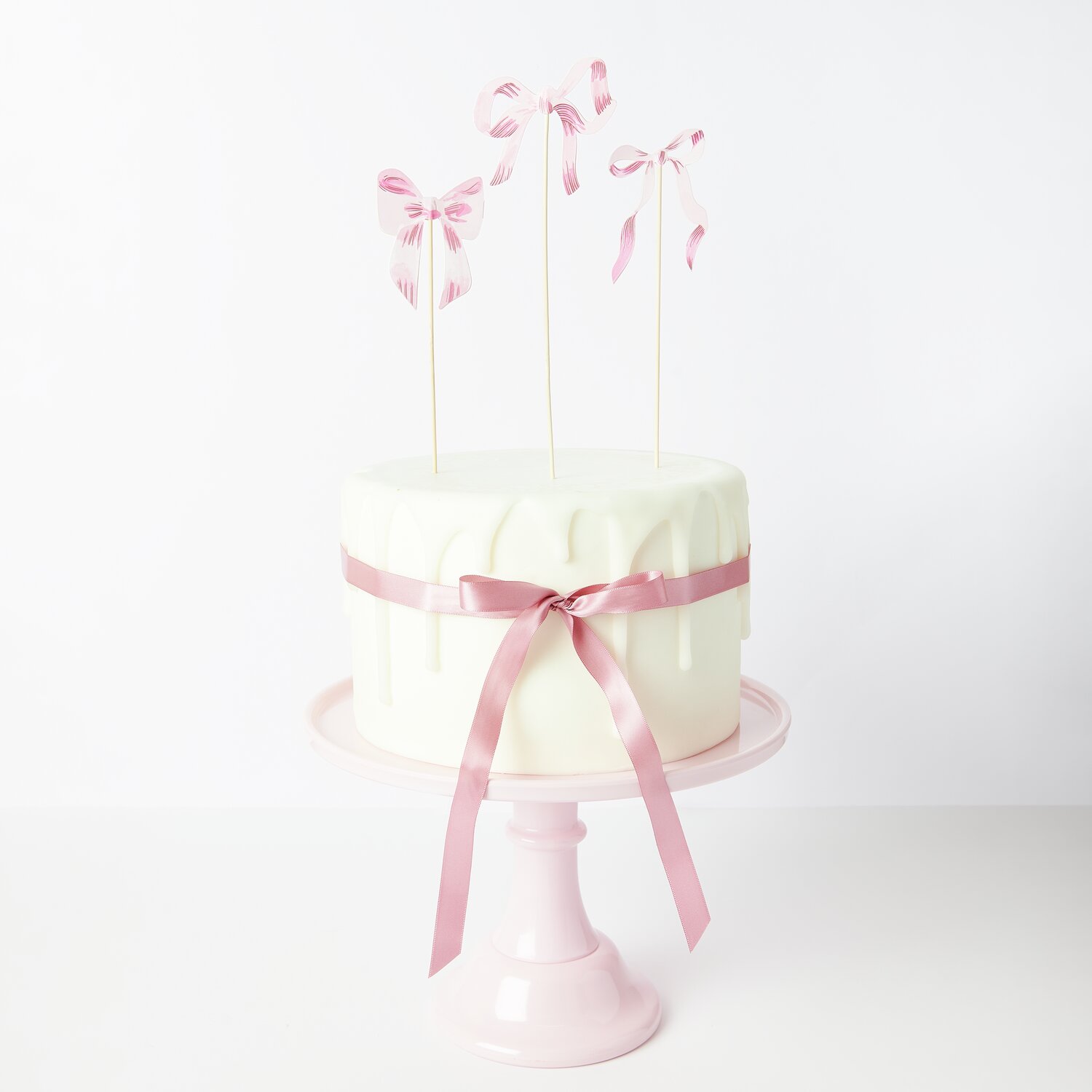 Picker Schleifen S Rosa: Weiße Torte mit rosa Schleifen und Bändern von Rico Design, dekorativ auf rosa Tortenständer.