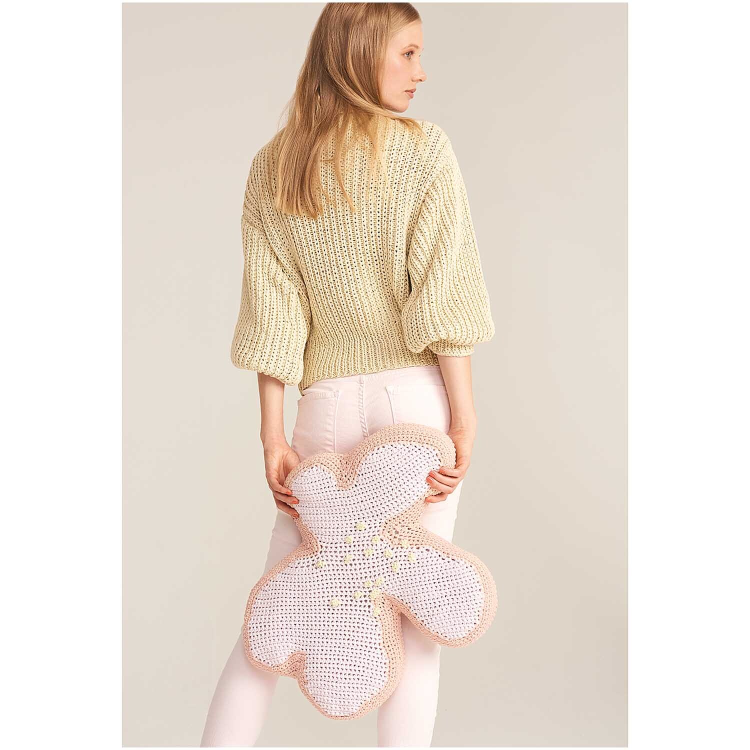 Fashion Jersey: Frau in pastellgelbem Strickpullover hält gehäkeltes Blumenaccessoire in Rosa.
