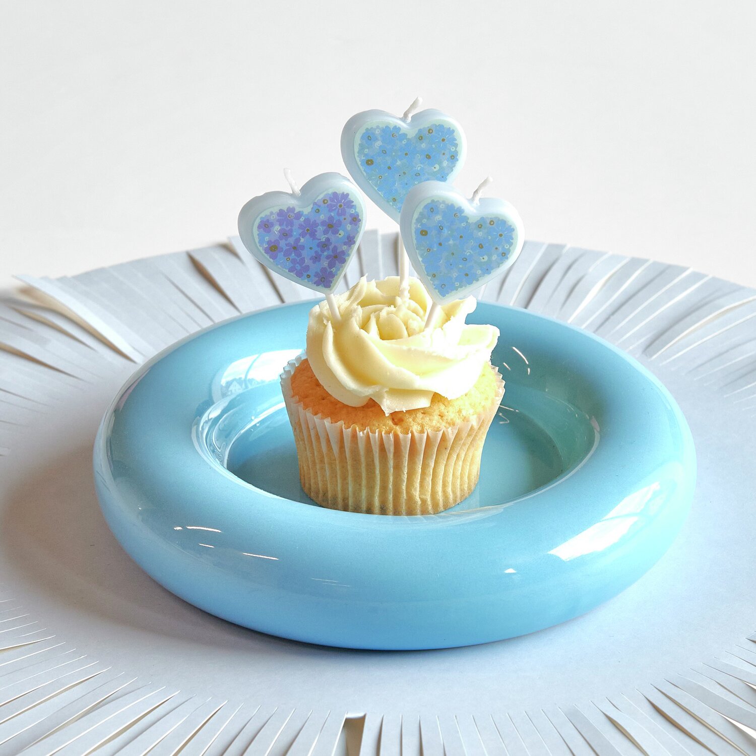 Kuchenkerzen Vergissmeinnicht auf Cupcake mit blauer Glasur, dekoriert auf einem blauen Teller.