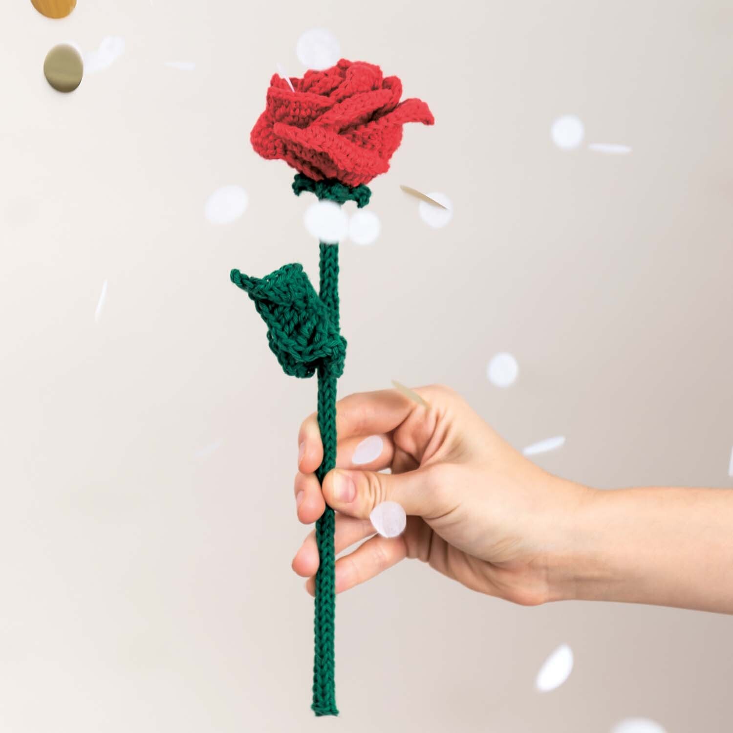 Häkelanleitung Ricorumi-Rose: Eine handgefertigte rote Rose mit grünem Stiel und Blättern, gehalten von einer Hand.