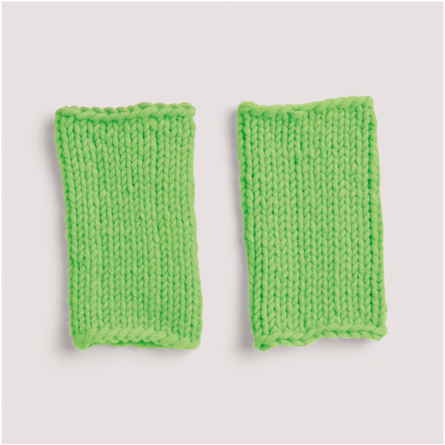 Strickset Stulpen Modell 03: Zwei leuchtend grüne, handgestrickte Stulpen auf hellem Hintergrund.
