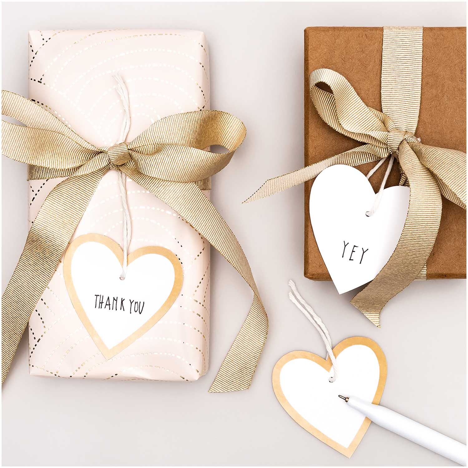 Paper Poetry Papieranhänger Herzen M 24 Stück, dekorativ auf Geschenken in Weiß-Gold mit Schleifen präsentiert.