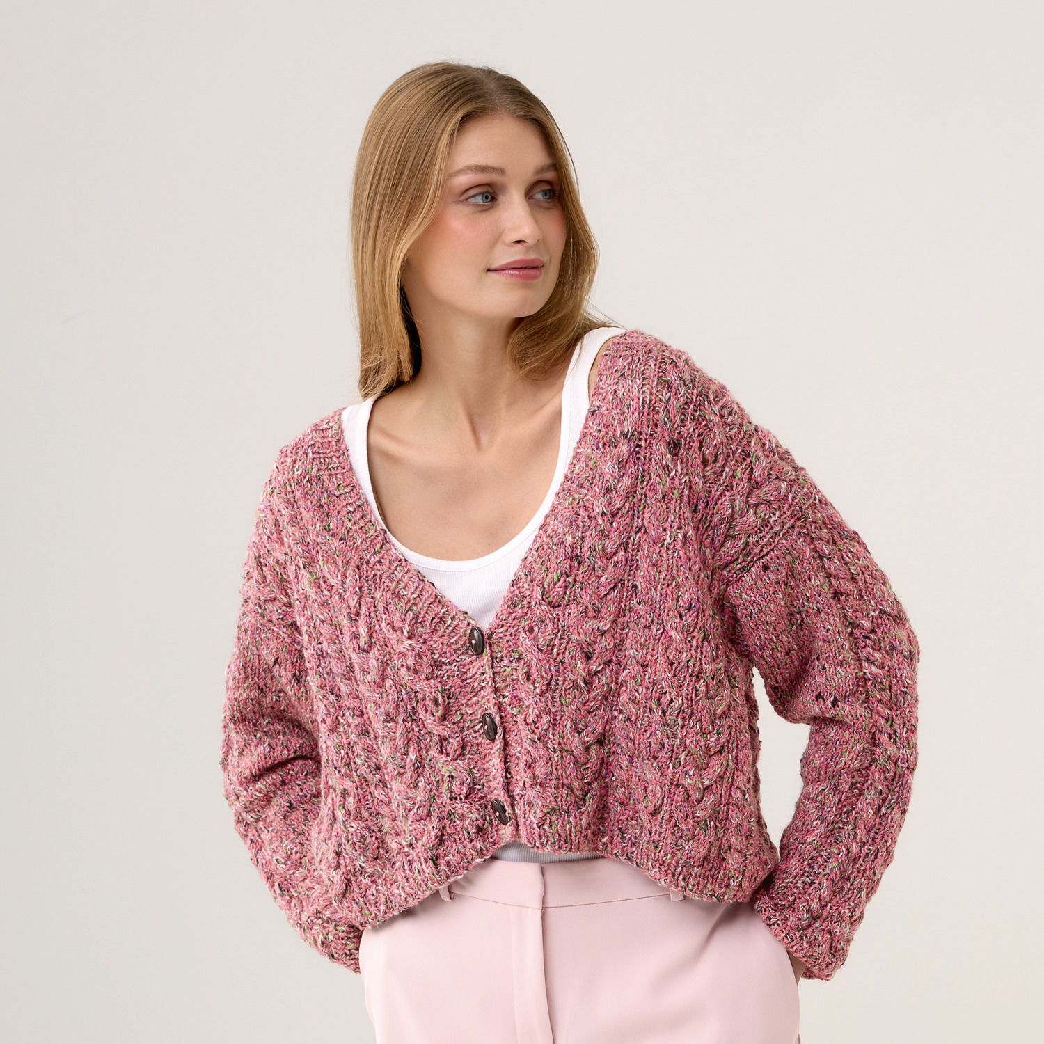 Strickset Jacke Modell 14: Frau trägt rosa Strickjacke mit Knöpfen, kombiniert mit weißem Top und rosa Hose.