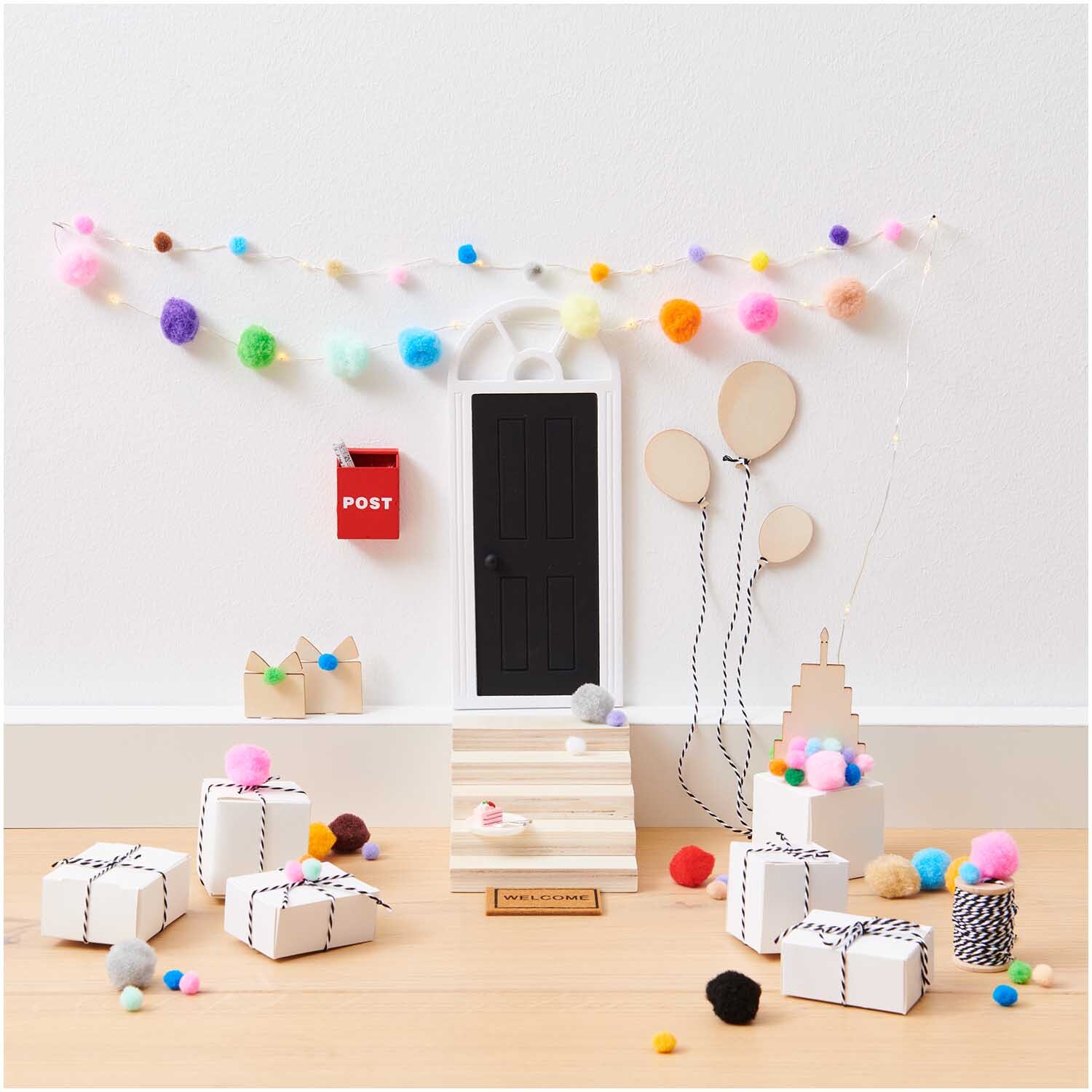 Miniatur Geschenkschachteln 6 Stück von Rico Design, dekoriert mit bunten Pompons und Luftballons vor einer kleinen Tür.
