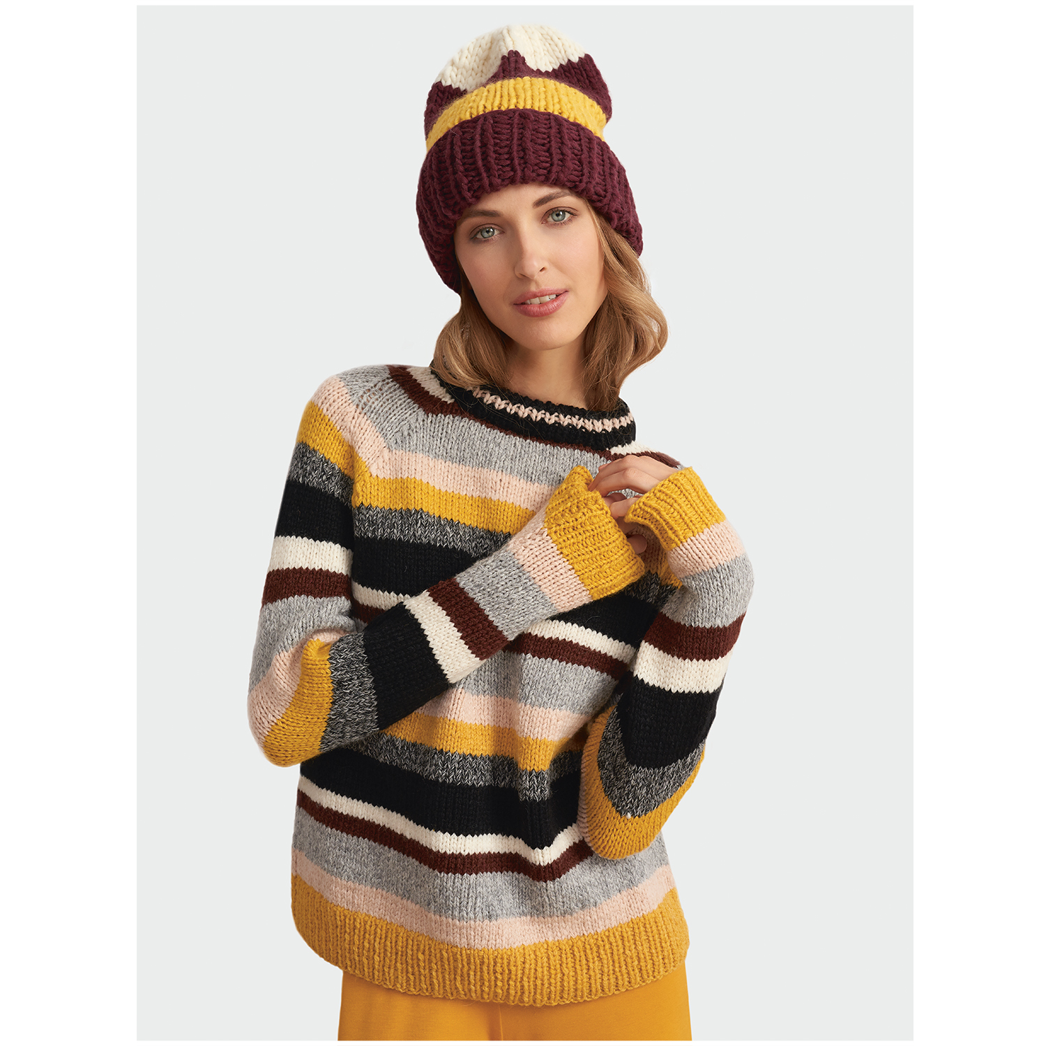 Fashion Alpaca Dream: Frau trägt gestreiften Pullover und Mütze in Gelb- und Brauntönen von Rico Design.
