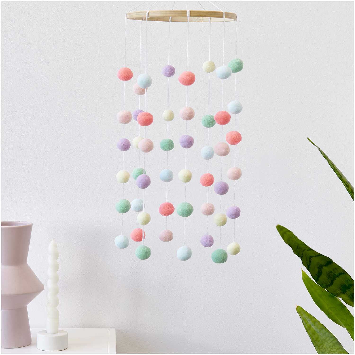 Bastelset Pompon Mobile pastell: Ein hängendes Mobile mit bunten Pompons von Rico Design, ideal zur Dekoration.
