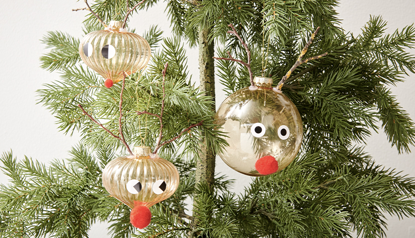 Bastelanleitung Christbaumkugeln im Scandi-Style: Goldene Kugeln mit Rentiergesichtern an einem grünen Tannenbaum.