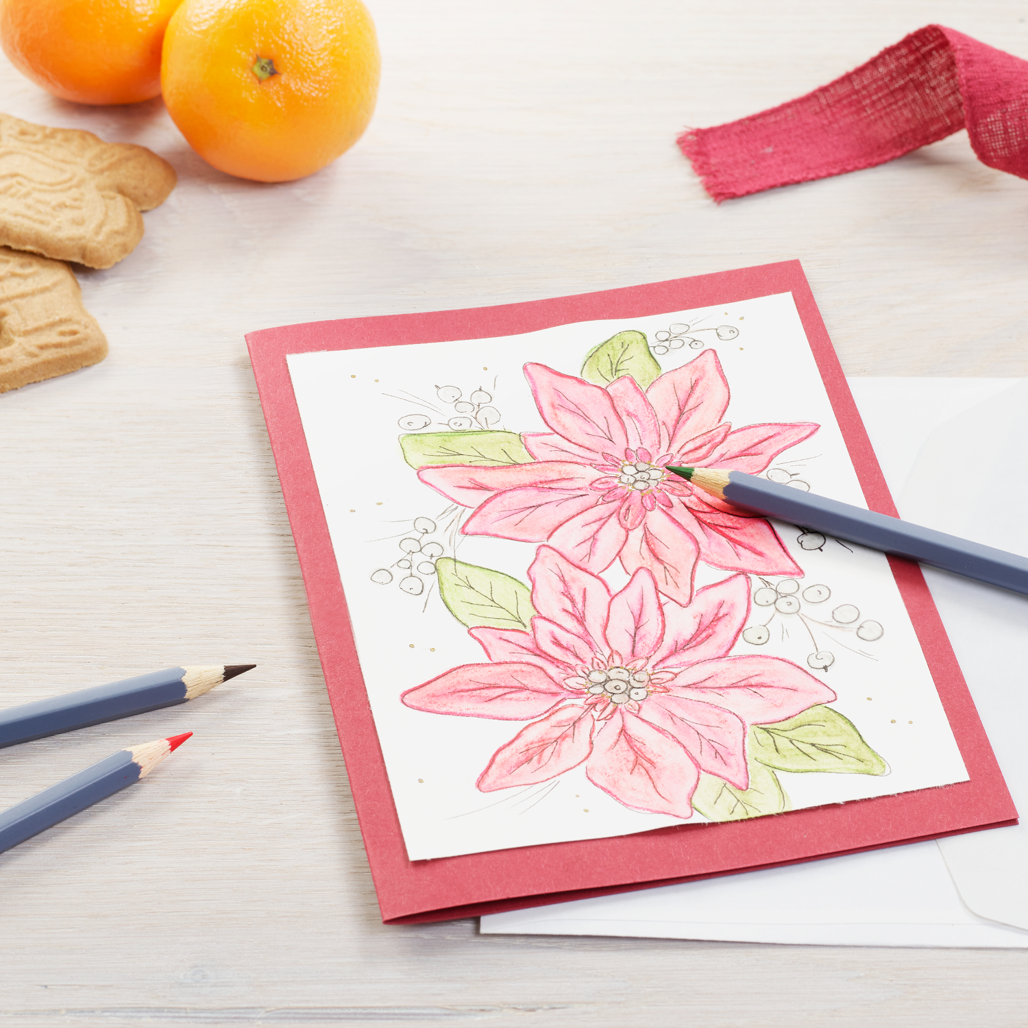 Goldfaber Aqua Aquarellstifte im Metalletui, 48-teilig: Rote Karte mit Blumenmotiv, umgeben von Stiften, Keksen und Orangen auf hellem Tisch.