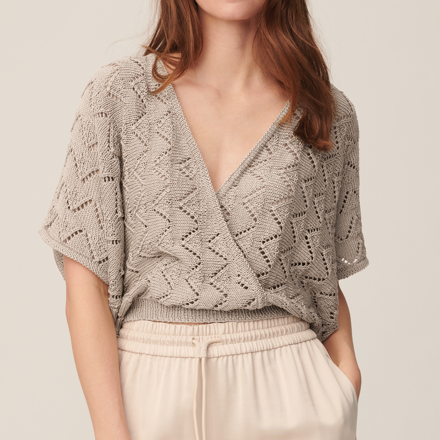 Strickanleitung Shirt aus Mille Fili: Frau trägt ein elegantes, beige Strickshirt mit Zickzackmuster und V-Ausschnitt.