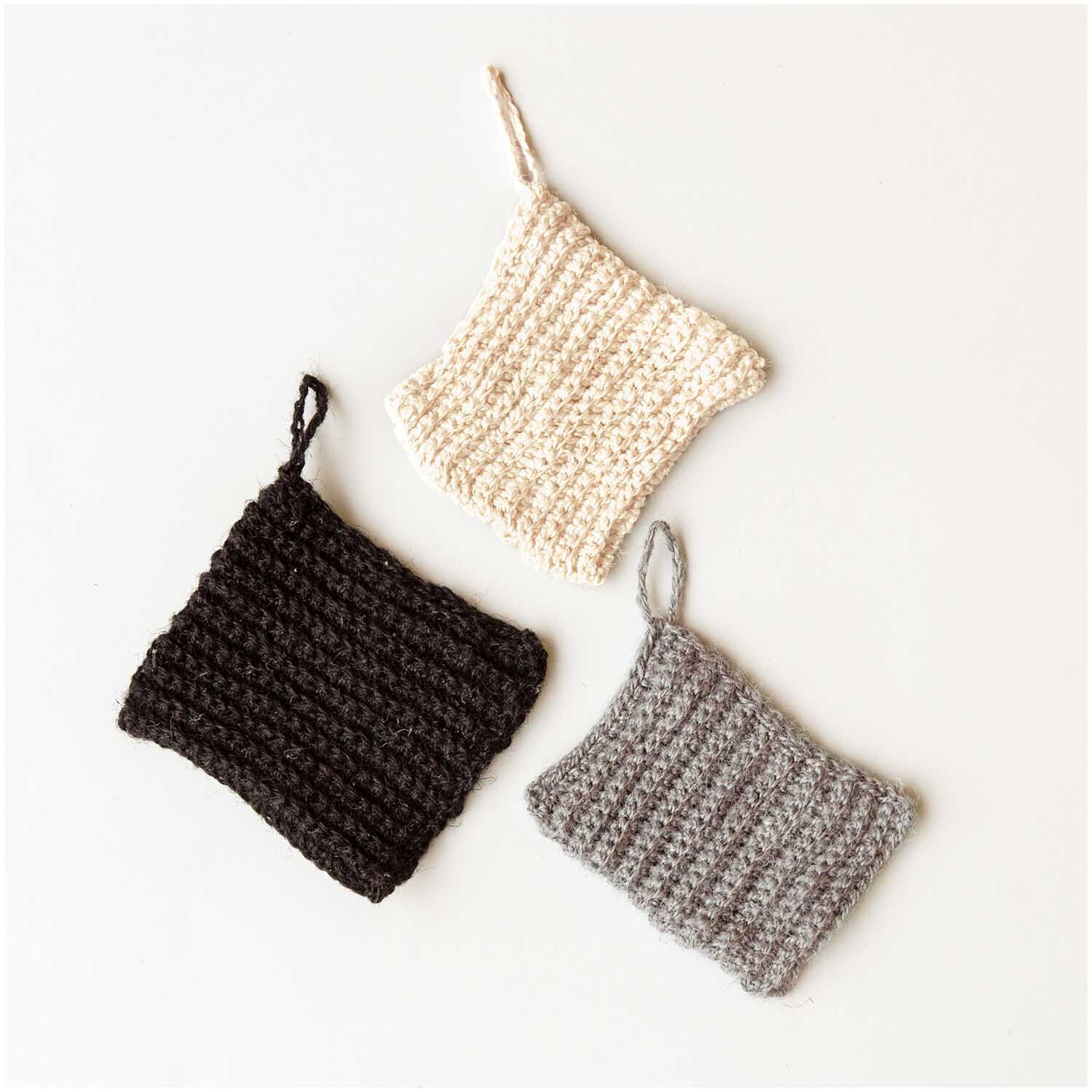 Creative Natur: Drei gestrickte Topflappen in Creme, Schwarz und Grau auf weißem Hintergrund.