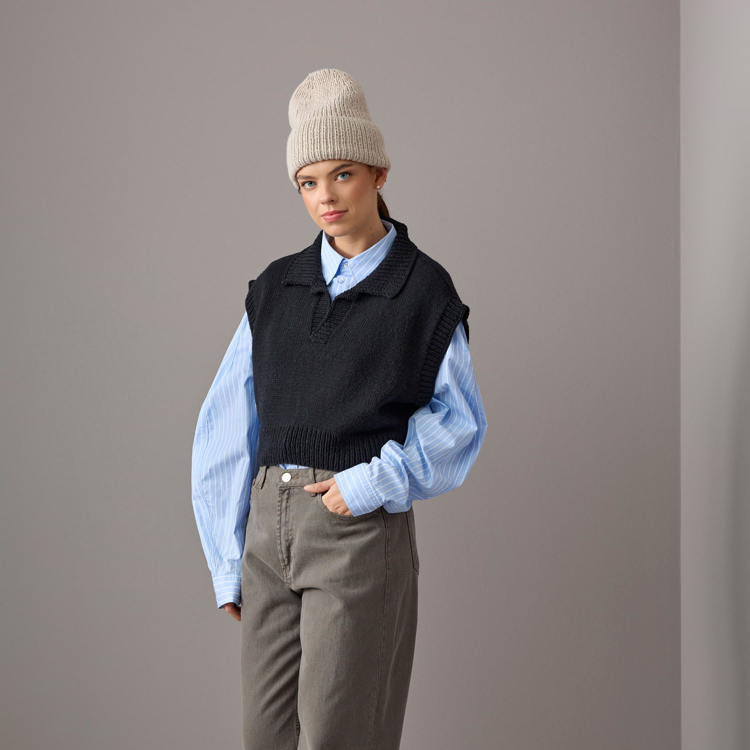Essentials Vegan Cashmere aran: Person trägt schwarzen Pullunder, blaue Bluse und beige Mütze. Marke: Rico Design.