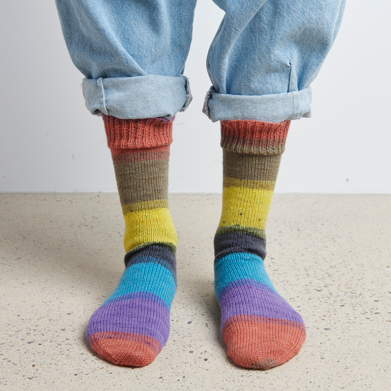 Superba Cashmeri Luxury Socks 4fädig in bunten Farben, getragen mit hochgekrempelten Jeans auf hellem Boden.