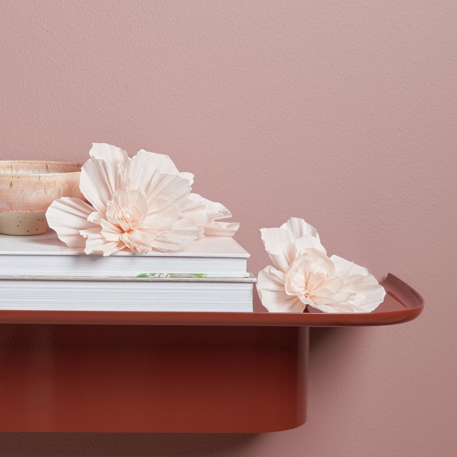 Krepppapier Blüten, Soft Pfirsich, 3 Stück, dekorativ auf einem roten Regal neben Büchern arrangiert.