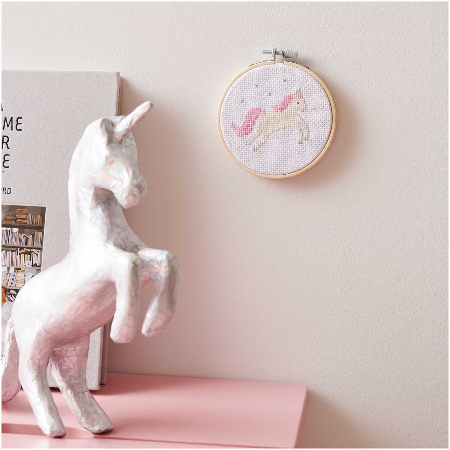 Stickpackung Mini Kit Einhorn Bild Ø 10cm an einer Wand, daneben eine weiße Einhornfigur.