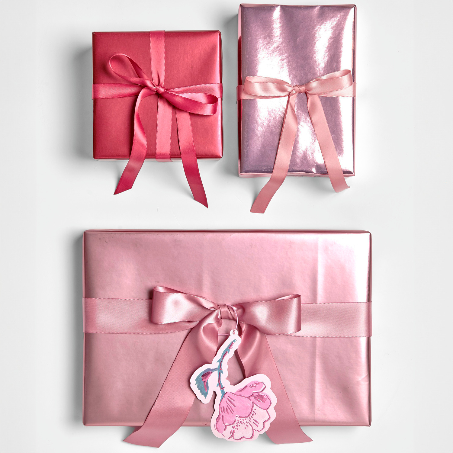Geschenkpapier Metallic Matt: Drei in Rosa und Rot verpackte Geschenke mit Schleifen, ideal für festliche Anlässe.