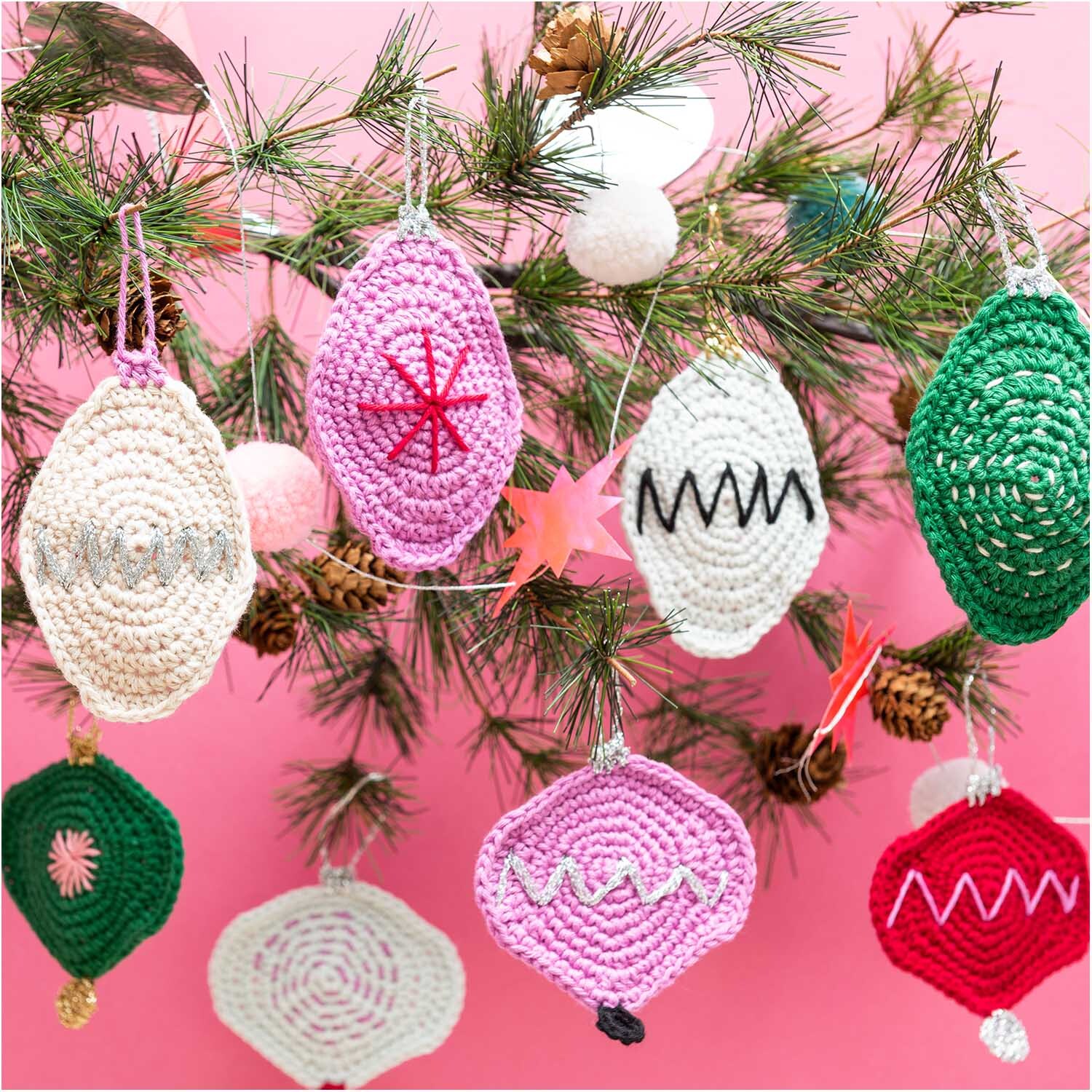 Creative Ricorumi dk: Gehäkelte Ornamente in verschiedenen Farben an einem Weihnachtsbaum vor rosa Hintergrund.