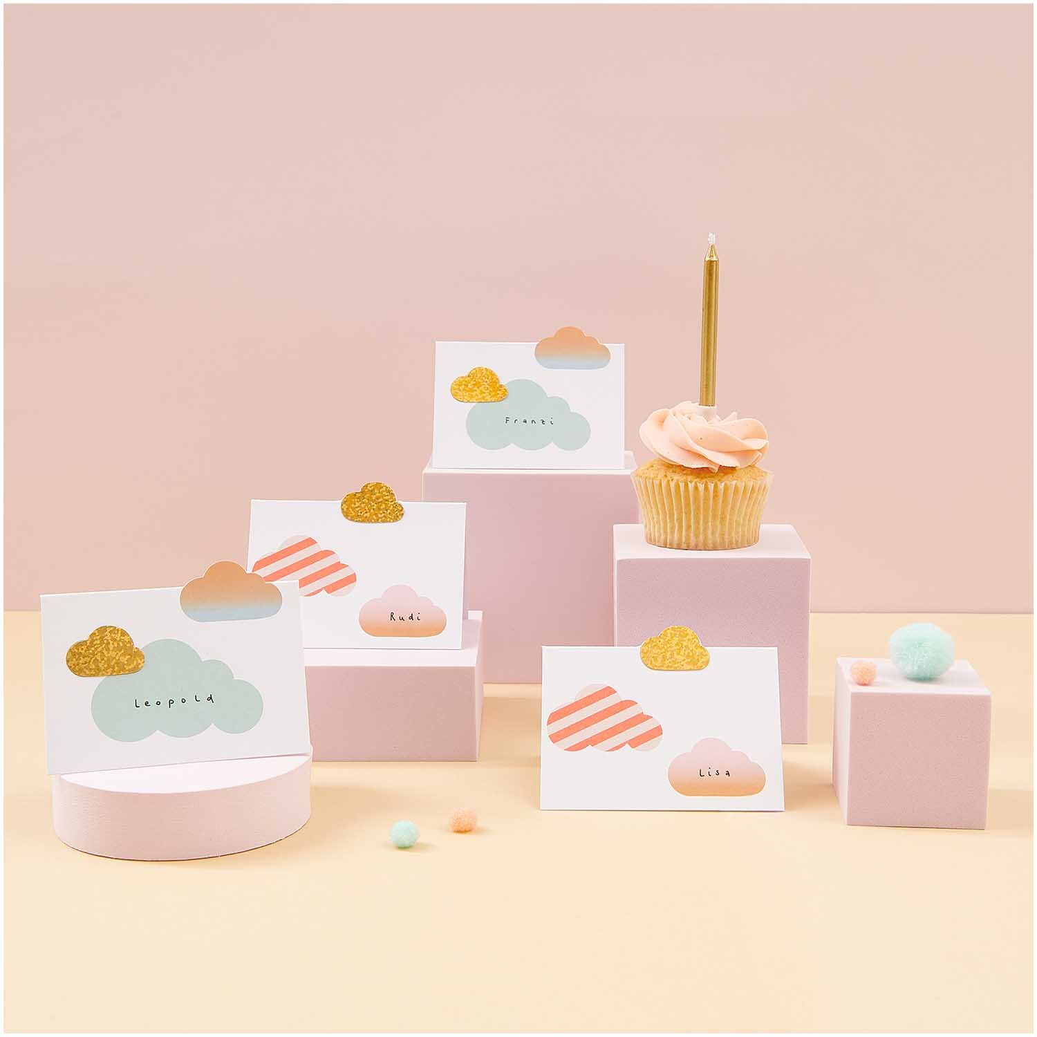 Paper Poetry Tischkarten mit Wolkenmotiv und pastellfarbenen Details, dekorativ arrangiert neben einem Cupcake. Ideal für festliche Anlässe.